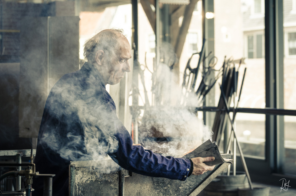 This man is considered a master in his profession since he has been working with glass for over forty years! He has great talent and his work is amazing! In this photo he is in the process of making a tea-light candle holder. When the picture was taken,&nbsp;he was just finished gathering the proper amount of molten glass for the final product. He continues spinning the rod that the glass is on to keep it in an even formation.&nbsp;He then takes these wetted papers to smooth it - but he isn’t finished with it yet.